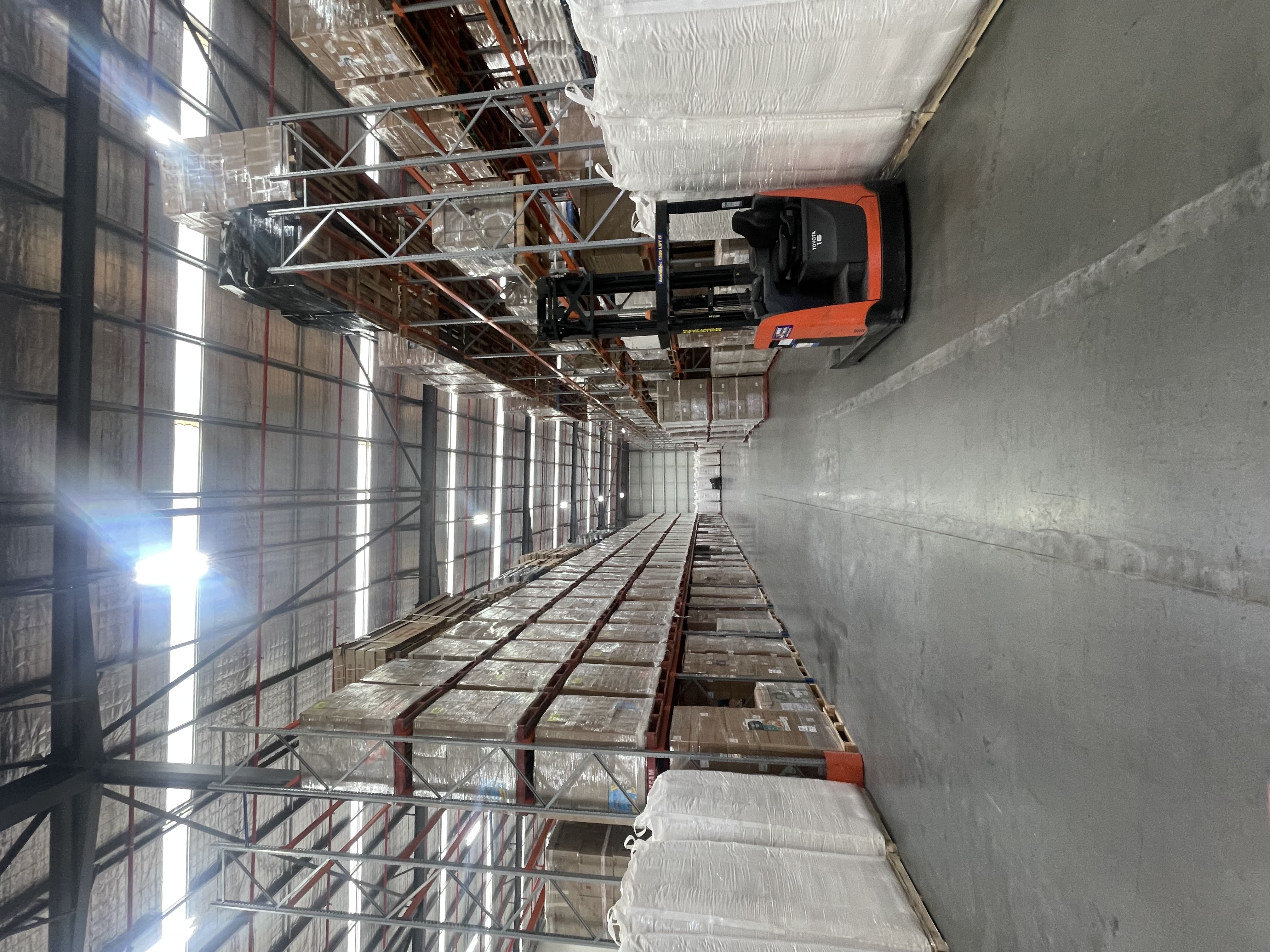A forklift in a warehouse aisle beside pallet racking