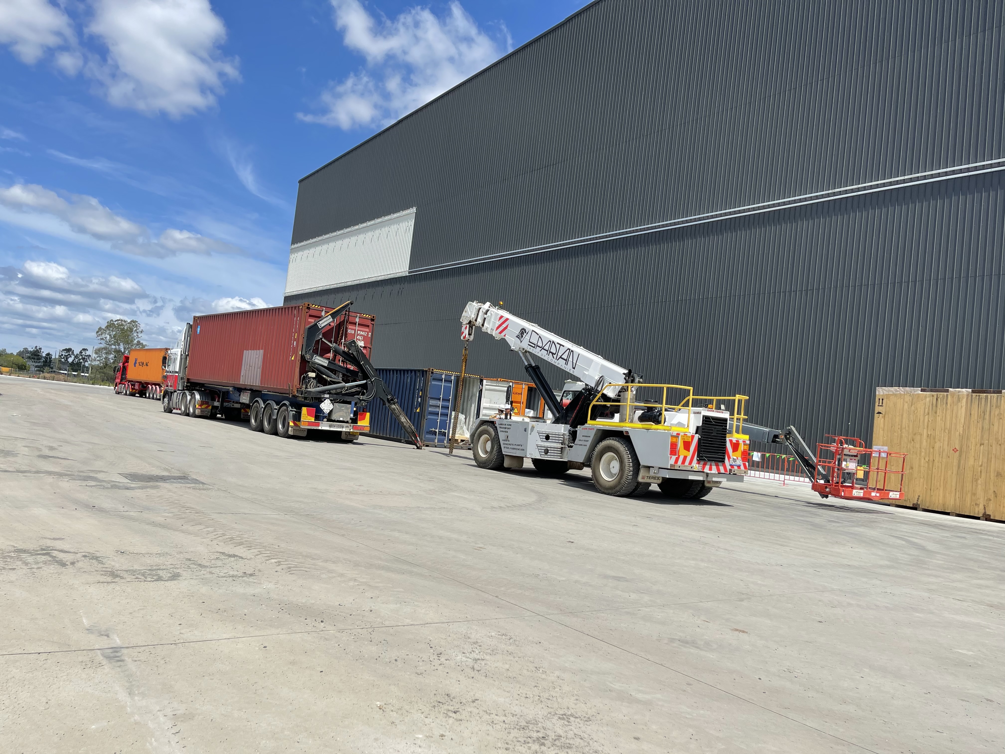 Container trucks and lifting equipment outside a warehouse